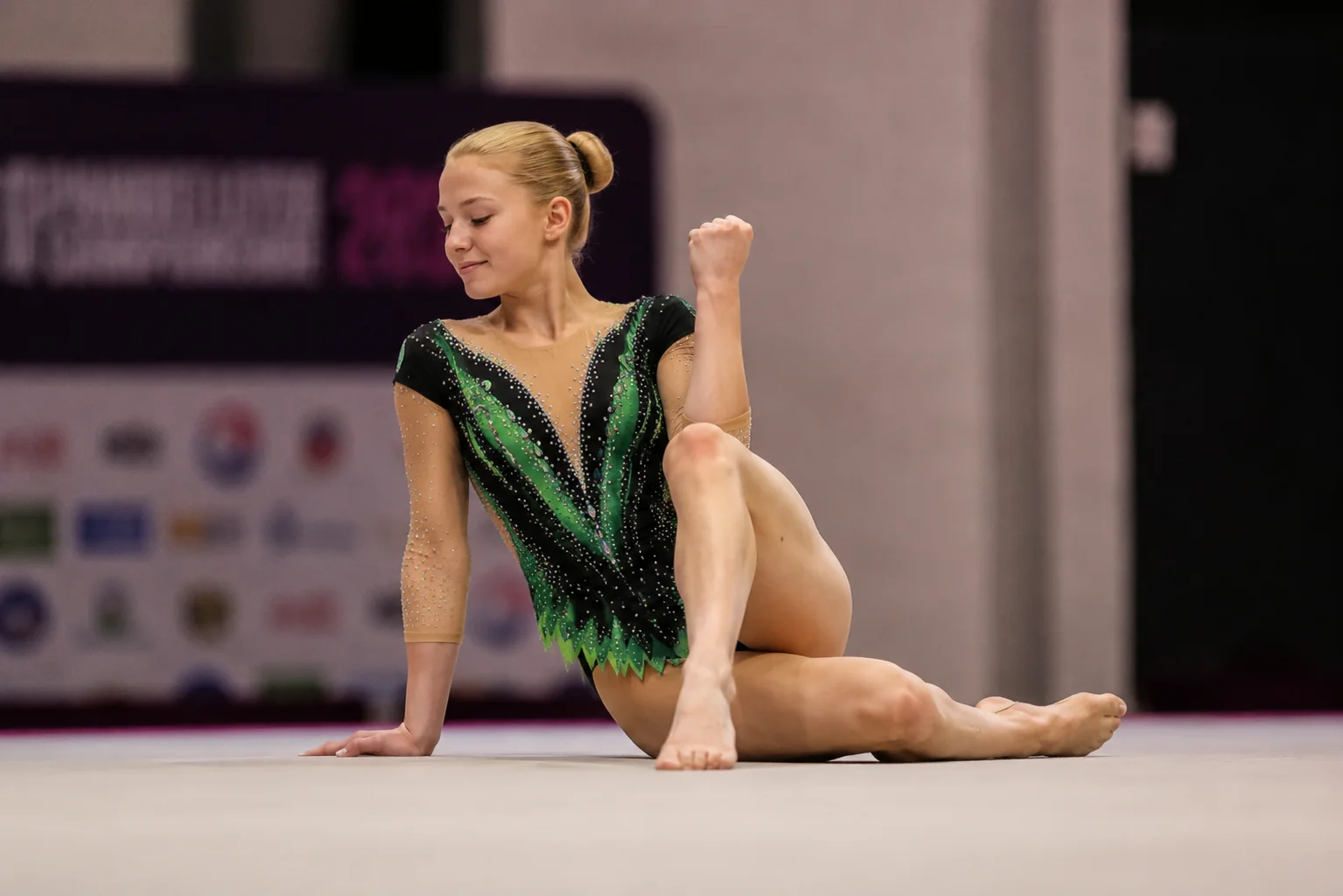 Gymnaste artistique portant un justaucorps vert et noir orné de cristaux sur un praticable